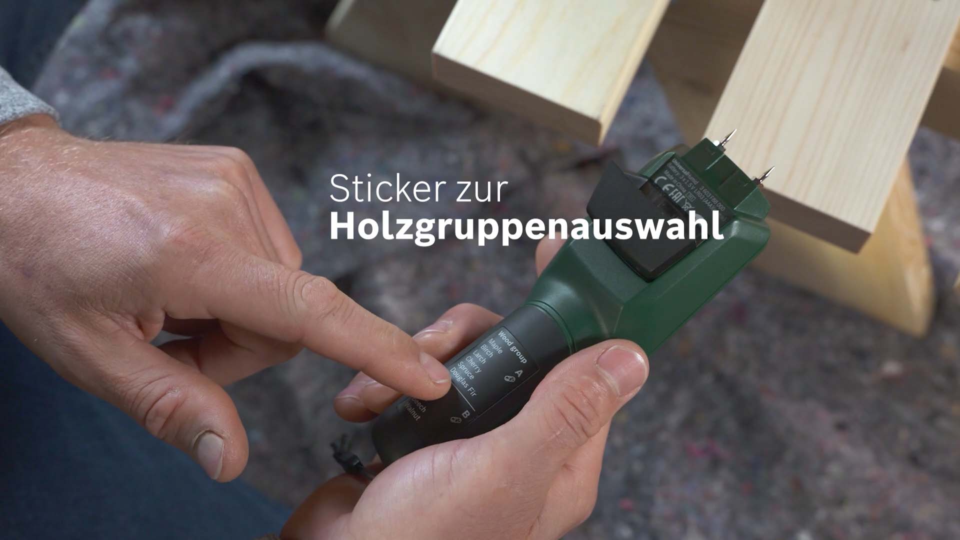 Darsteller zeigst auf dem Universal Humid Werkzeug von Bosch auf den Sticker zu Holzgruppenauswahl.